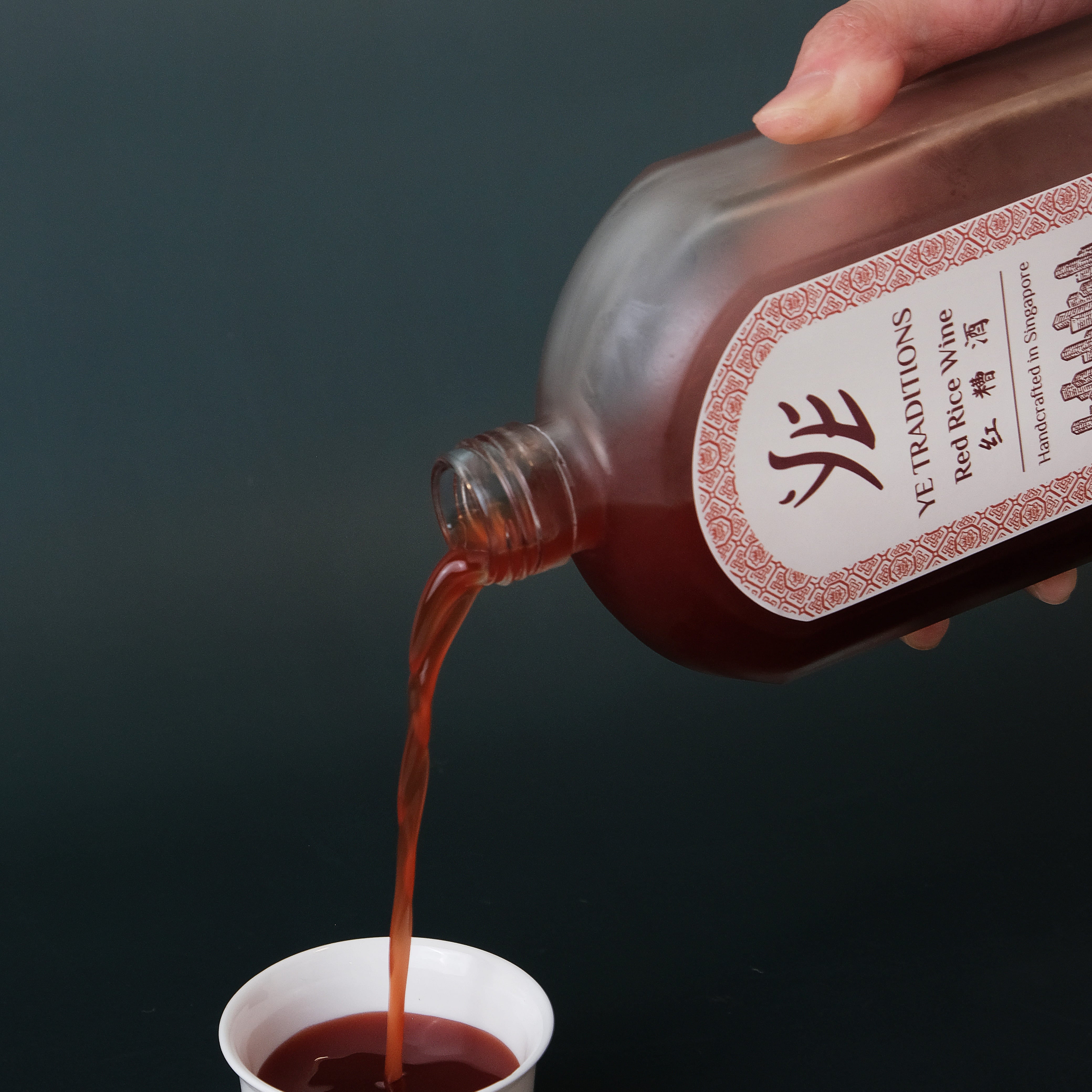 hand pouring chinese red rice wine into a cup